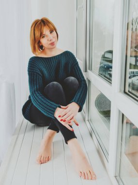 Kızıl saçlı kız pencere eşiğinde oturuyor..