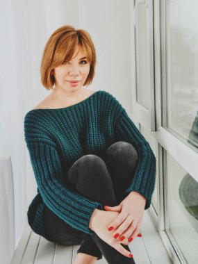 Kızıl saçlı kız pencere eşiğinde oturuyor..