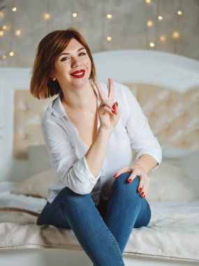 Kızıl saçlı, kırmızı dudaklı, büyük bir yatakta poz veren kız..