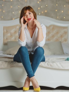 Kızıl saçlı, kırmızı dudaklı, büyük bir yatakta poz veren kız..