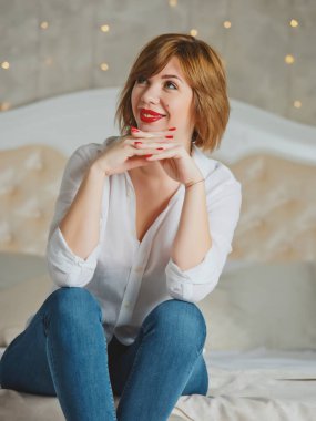 Kızıl saçlı, kırmızı dudaklı, büyük bir yatakta poz veren kız..