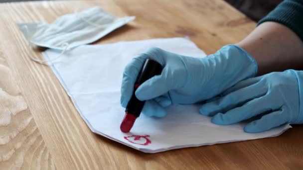 Kobiety w niebieskich rękawiczkach piszą "kwarantanna" czerwoną szminką na białym prześcieradle. Zbliżenie. — Wideo stockowe