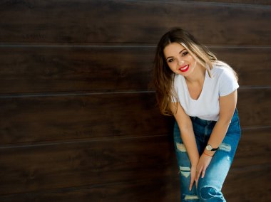 Beyaz tişörtlü ve kot pantolonlu, kahverengi arka planda genç, çekici bir kız..