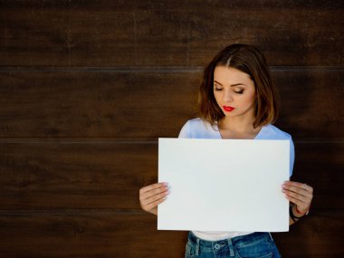 Üzgün genç kız, elinde boş tabela var. Ahşap arkaplan.