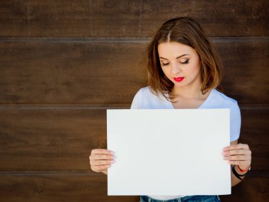 Üzgün genç kız, elinde boş tabela var. Ahşap arkaplan.