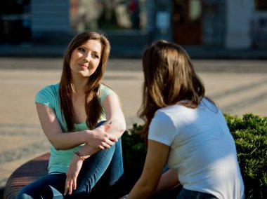 İki kız arkadaş parktaki parkta oturup sohbet ediyorlar..