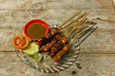 Baharatlı soslu ızgara tavuk satay ve ahşap masadaki salatalık geleneksel Endonezya yemeği. Sahilde..