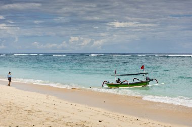 Pandawa plajı, Bali, Endonezya. - 2 Mart 2017 'de kız arka planda bir balıkçı teknesiyle sahilde yürüyor..
