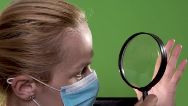 Uma rapariga com uma máscara médica olha para a mão através de uma lupa. Retrato de close-up na tecla chroma . — Vídeo de Stock