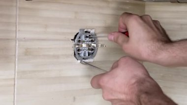 İki tornavidayla elektrik prizini tamir eden erkek eller. Yakın plan..