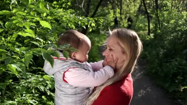 Genç anne küçük kızını kollarında tutuyor. Ormanda yürü. Anneler günü konsepti. — Stok video