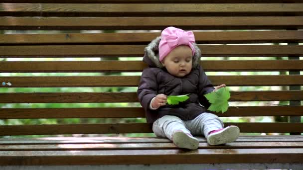 Liten flicka sitter på en parkbänk och ler mot kameran. — Stockvideo