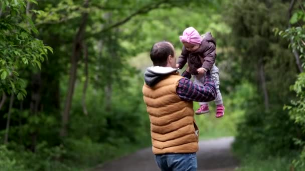 Ένας άντρας παίζει με την κόρη του σε ένα πάρκο, στριφογυρίζοντας στον αέρα στην αγκαλιά της. Αργή κίνηση — Αρχείο Βίντεο
