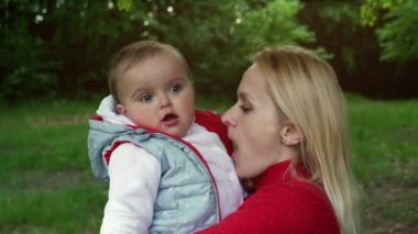 Bir yaşındaki kızını kucağında tutan genç bir anne. Yakın plan. Parkta bir yürüyüş..
