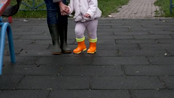 母と娘はゴムブーツで遊び場を歩いています. — ストック動画