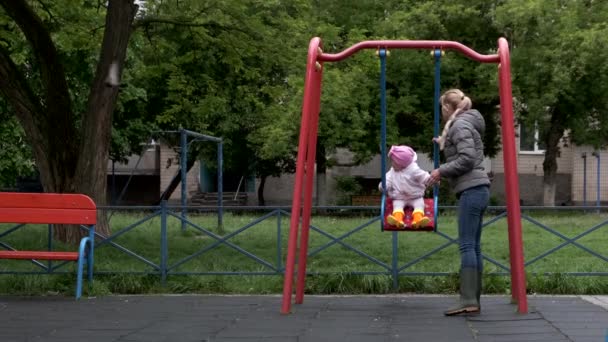 En ung mor rullar sin dotter på en gunga. — Stockvideo