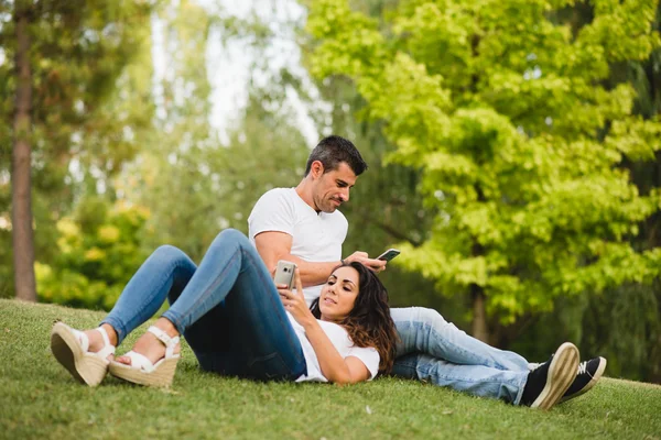 Пара насолоджується дозвіллям у парку зі своїми смартфонами — стокове фото