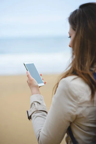 Γυναίκα μηνυμάτων στο smartphone χειμώνα στην παραλία — Φωτογραφία Αρχείου