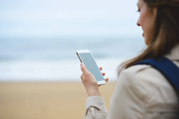 Kobieta, wiadomości na smartfonie na zimowe na plaży — Zdjęcie stockowe