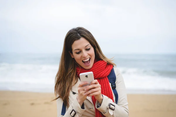 Mujer sorprendida mensajes de texto en el teléfono inteligente en la playa en otoño — Foto de Stock