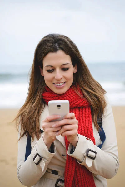 Vrolijke vrouw texting op smartphone op het strand op de herfst — Stockfoto