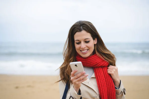 Veselá žena textilie na smartphone na pláži na podzim — Stock fotografie
