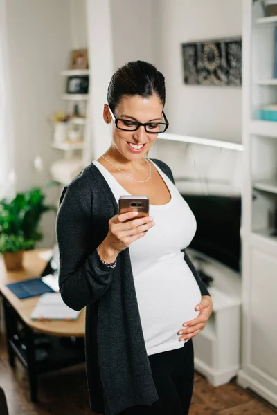 Casual zwangere vrouw smartphone thuis gebruiken — Stockfoto