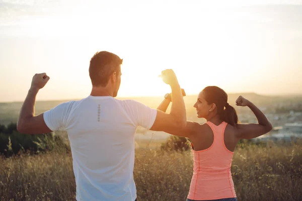 Coppia di corridori che lexing bicipiti verso il sole — Foto Stock