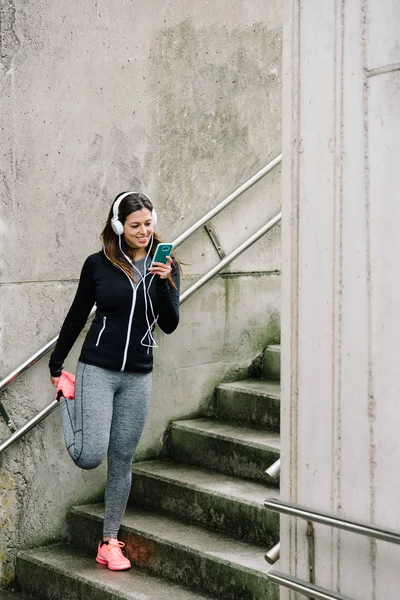 Sporty woman texting on smartphone and stretching — Stock Photo, Image