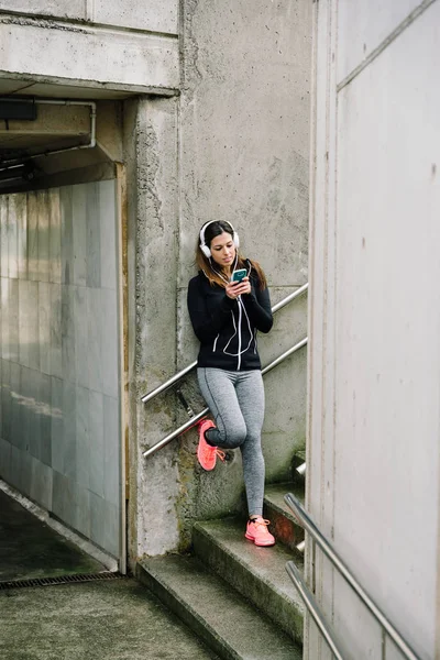 Sporty woman with headhphones texting on smartphone — Stock Photo, Image