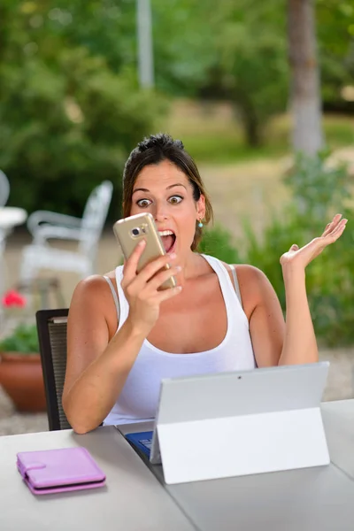 Mujer casual sorprendida con portátil y teléfono inteligente fuera —  Fotos de Stock