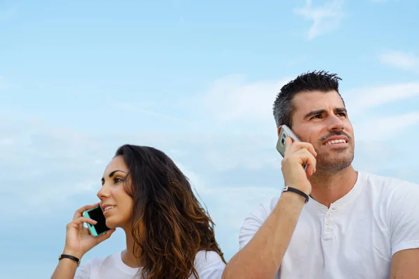 Man och kvinna på talar på mobiltelefoner mot himmel bakgrund — Stockfoto