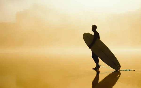 Puslu bir kentsel kumsalda onun surfboard holding sörfçü — Stok fotoğraf