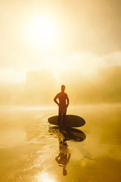 Surfista con su tabla de surf en una playa urbana brumosa —  Fotos de Stock