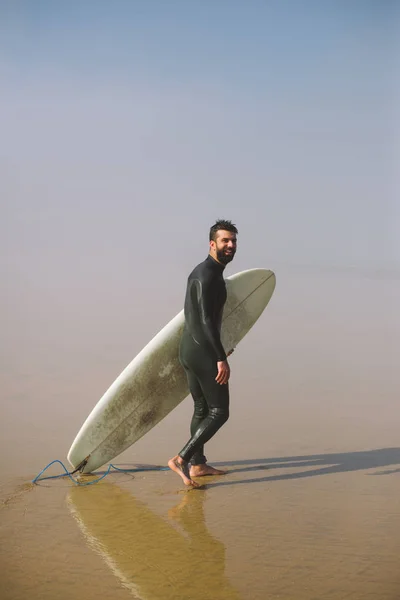 Серфер з дошкою для серфінгу на туманному пляжі — стокове фото