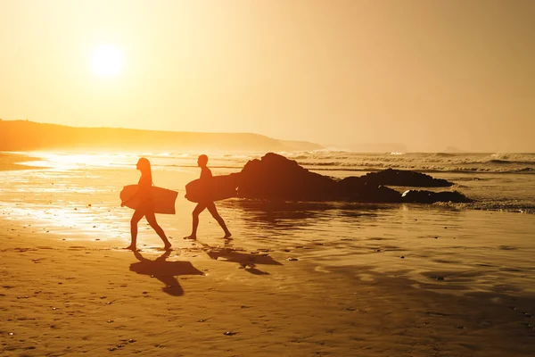 Pareja de surfistas en una puesta de sol dorada en la playa —  Fotos de Stock