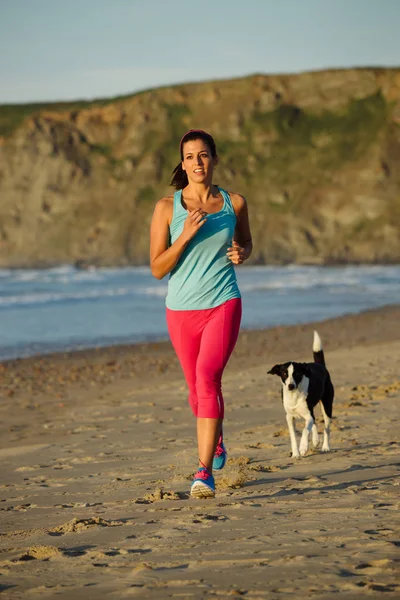 Zdravá žena a pes běží spolu na pláži — Stock fotografie