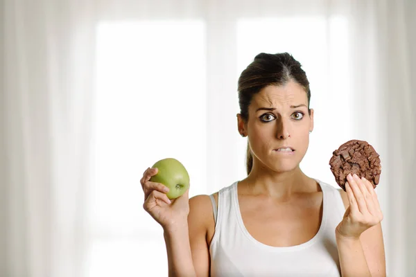 Woman choosing between a healthy apple and a chocolate chip cook — Stock Photo, Image