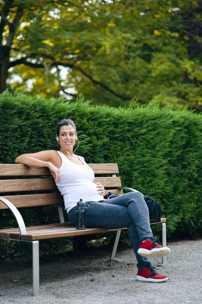 Γυμναστήριο έγκυος γυναίκα κάθεται σε ένα παγκάκι — Φωτογραφία Αρχείου