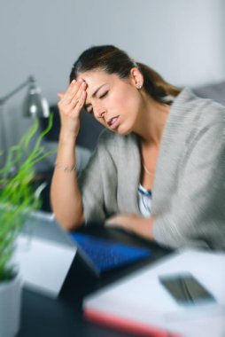 Sick dizzy young woman suffering headache while working on her laptop at home. clipart