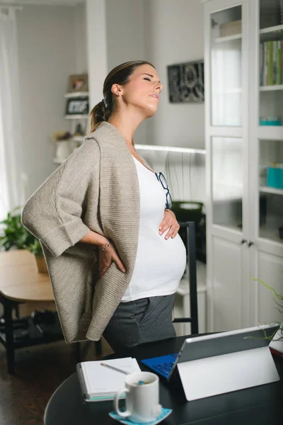 怀孕的妇女在家里用她的可换笔记本电脑工作时 背痛得很厉害 怀孕健康问题概念 — 图库照片