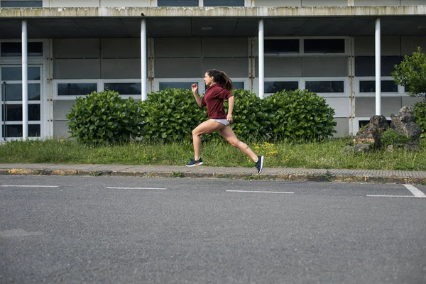 アスファルトの道路上で良い技術で実行している女性アスリートのサイドビュー 外での短時間トレーニングでスポーティ女性 — ストック写真