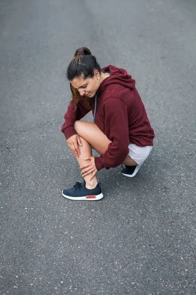 痛みを伴うランニング傷害 アスファルトのトレーニング中に足首や腱炎の病変に苦しんでいる女性ランナー — ストック写真