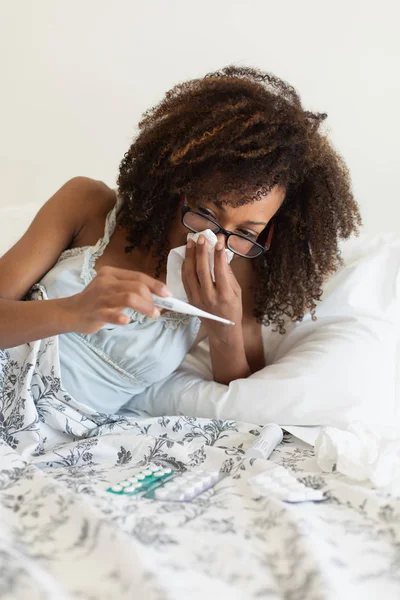 患感冒或流感的年轻妇女躺在床上用温度计量体温 — 图库照片