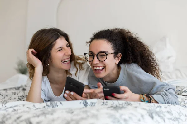 Dos Jóvenes Lesbianas Ríen Mientras Usan Sus Teléfonos Inteligentes Cama — Foto de Stock