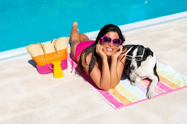 プールで楽しい夏に一緒に幸せな女性とかわいい犬の日光浴 美しい女の子と彼女のペット身に着けているサングラスと楽しい休日にプールサイド — ストック写真