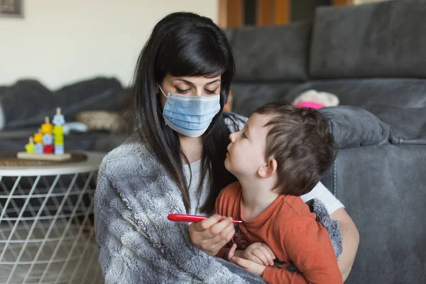 Worried woman with face mask suffering coronavirus symptoms at home. Mother and son at home on Covid-19 quarantine.