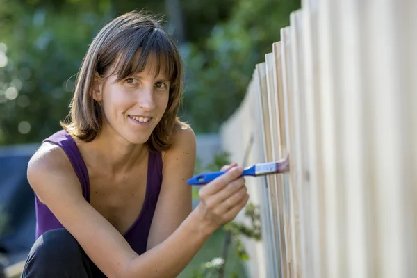 Lachende vrouw schilderij een tuin hek — Stockfoto