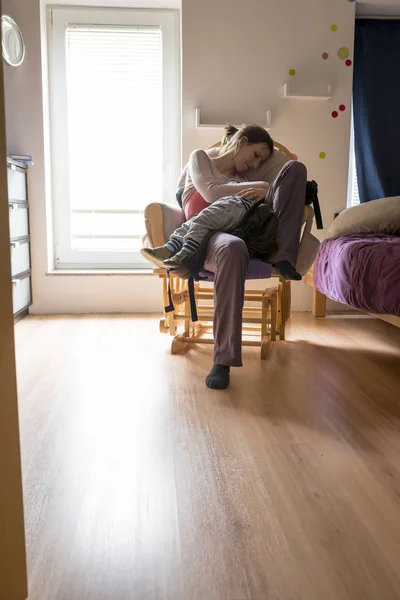 Giovane madre seduta e riposante in una sedia a dondolo che la tiene — Foto Stock