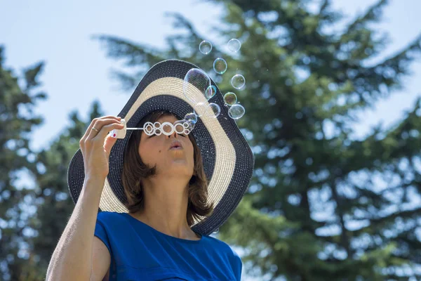 Stylish woman in a straw sunhat blowing bubbles — Stock Photo, Image